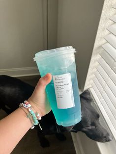 a person holding up a plastic cup with blue liquid in it and a black dog behind them