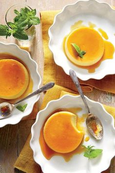 two white bowls filled with orange custard soup on top of a wooden table