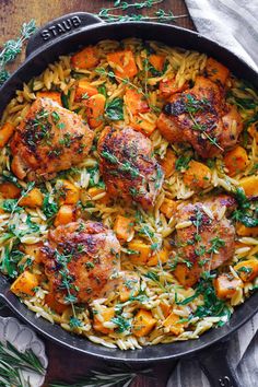 a skillet filled with chicken, pasta and carrots on top of a wooden table