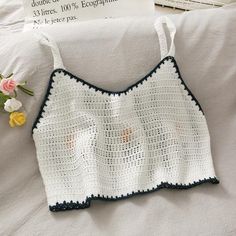 a crocheted white top with blue trim and flowers on the bed next to it