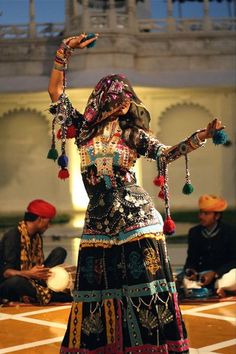 a woman dressed in an elaborately decorated outfit performing a dance with other people around her