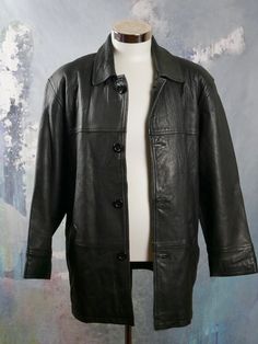 "This 1990s black leather coat has a wing collar and padded shoulders, and closes in the front with four black buttons. The coat has two hip pockets on the front, and is fully lined in a black satin rayon fabric (with two inner zippered pockets). Note that this is a \"short\" size (46S). Brand label: Dönmez Size: 46S US/UK Material: Genuine Leather Chest = 48 inches (121.92cm)(This is a Size 46S US/UK; the extra 2 inches here allow for what you wear under.) Shoulder Width = 21 inches (53.34cm) S Classic Black Leather Long Coat, Classic Black Long Leather Jacket, Classic Black Leather Jacket With Button Closure, Vintage Black Leather Jacket With Button Closure, Classic Black Leather Jacket With Double Button Closure, Black Vintage Leather Jacket With Button Closure, Black Vintage Outerwear With Double Button Closure, Winter Leather Outerwear With Snap Closure, Vintage Black Outerwear With Snap Buttons