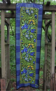 a blue and green quilt hanging from a wooden fence