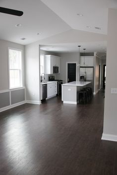 an empty living room with hard wood flooring and white appliances in the kitchen area