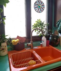 an orange sink sitting under a window in a green counter top next to potted plants