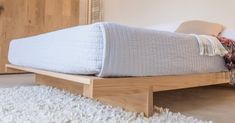 a bed that is made up and sitting on a white rug in a room with wood furniture