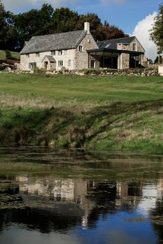 a large stone house sitting on top of a lush green field next to a river