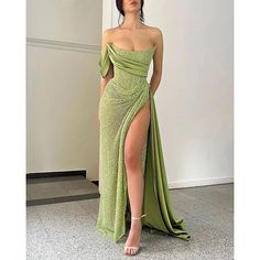 a woman in a green dress standing next to a wall with her legs slited