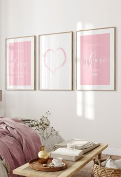 three framed pink and white posters on the wall above a bed in a room with a wicker coffee table