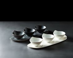 five black and white bowls sitting on a tray next to each other, with one empty bowl in the middle