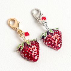 two strawberry charms are hanging on a white surface with red and green crystals in them