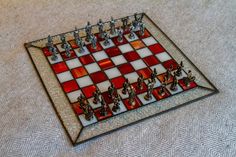 a glass chess board with red and white squares on it's sides, sitting on a carpeted floor