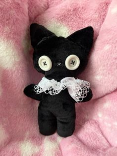 a black cat with big eyes sitting on a pink blanket