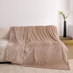 a living room with a couch covered in a blanket next to a vase on the floor