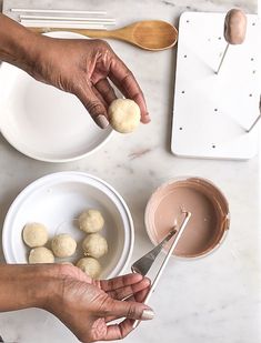 two hands are holding doughnuts in front of a bowl of chocolate and spoon