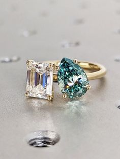 two different colored diamond rings sitting on top of each other, one with a green and white stone in the middle