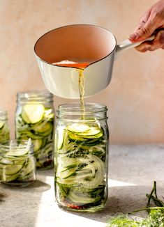 a person pours dressing into a jar filled with cucumbers and herbs to make pickles