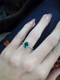 a close up of a person's hand with a green ring on their finger