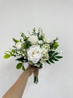 a hand holding a bouquet of white roses and greenery on a white background with copy space