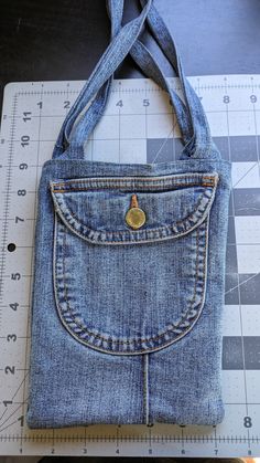 a purse made out of jeans sitting on top of a cutting board next to a ruler