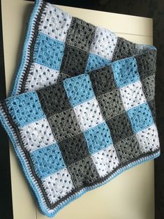 there is a crocheted blanket that has squares on it and blue, gray, and white