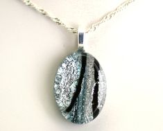 a glass pendant is hanging from a silver chain on a white surface with black stripes