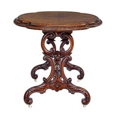 an ornately carved wooden table with wheels on the legs and a circular top,