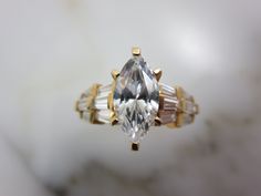 "A vintage 14k gold and CZ engagement ring, with accent stones set in the wide shoulders of the ring. Marked \"14k MUS CZ\" and acid tested, also marked with something else I cannot make out. A US size 9. Actual packaging will vary depending on item/s purchased and tape pattern available. Props/boxes shown in photos are for display purposes only, not included in this listing. As always, satisfaction is guaranteed. Thanks for shopping Vintage In Bloom More rings: http://www.etsy.com/shop/VintageI Art Deco Marquise Diamond Ring With Center Stone, Vintage Diamond Ring With Baguette Cut Center Stone, Timeless Diamond Cut Topaz Ring For Anniversary, Gold Marquise Gemstone Wedding Jewelry, Wedding Topaz Ring With Diamond Accents, Baguette Cut, Wedding Topaz Ring With Center Stone And Baguette Cut, Baguette Cut Topaz Ring For Wedding Vvs Clarity, Baguette Cut Topaz Ring With Diamond Accents For Wedding, Timeless Marquise Cut Stone Jewelry