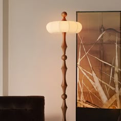 a floor lamp sitting next to a couch in a living room with a painting on the wall