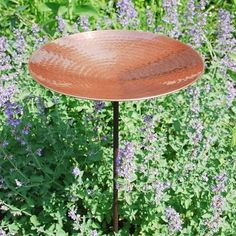 a bird bath sitting on top of a metal pole in front of purple and green plants