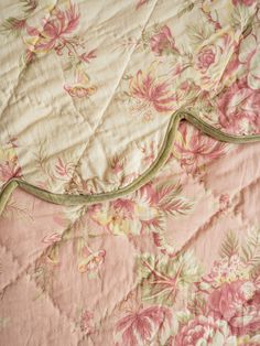 an unmade bed with pink and green floral bedspread on top of it