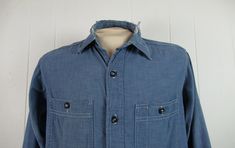 "Vintage 1940s work shirt. Made of cotton chambray. Color is medium blue. Has a button down front, button cuffs, two chest pockets and triple stitched seams. Hercules work clothing by Sears. Size medium. Actual measurements are: 43\" at the chest 42\" at the waist 16\" shoulder seam to shoulder seam 25\" shoulder seam to cuff 32\" overall length In good condition with a worn through collar and some minor paint spots." Pre-washed Cotton Button-up Shirt, Pre-washed Unstructured Button-up Shirt, Vintage Washed Button-up Top, Vintage Unstructured Collared Tops, Vintage Unstructured Shirt For Workwear, Unstructured Vintage Shirt For Work, Vintage Washed Blue Tops With Button Closure, Unstructured Collared Vintage Tops, Vintage Washed Blue Tops With Pockets