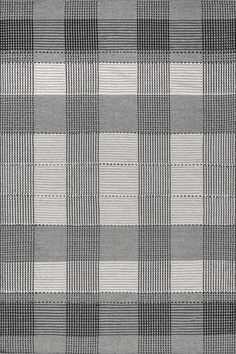 a gray and white checkered pillow on top of a wooden floor with an area rug underneath it