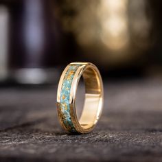 a wedding ring with gold and turquoise stone inlayed to the side, sitting on top of a table