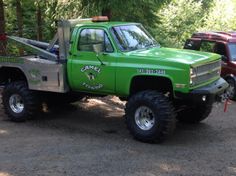 a green pick up truck parked on top of a dirt road next to some trees