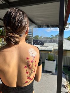 a woman with a tattoo on her back standing in front of a building and looking at the sky