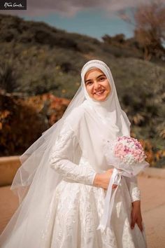 a woman in a white wedding dress holding a bouquet of flowers and smiling at the camera