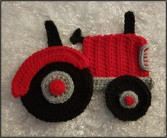 a crocheted red and black toy tractor laying on top of a white blanket