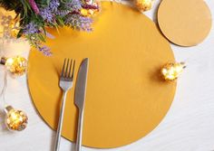 a place setting with flowers, candles and silverware on a yellow round tablecloth