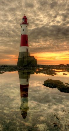 a red and white lighthouse sitting on top of a body of water under a cloudy sky