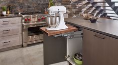 a kitchen scene with focus on the mixer in the center and stairs leading up to the upper floor