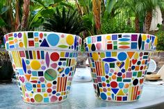 two large colorful pots sitting on top of a table next to palm trees and water