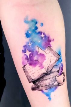 a watercolor tattoo with an open book and stars on the left side of the arm