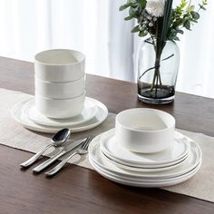 the table is set with white dishes and silverware, along with flowers in a vase