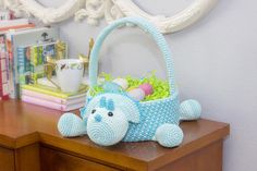 a blue crocheted elephant sitting on top of a wooden table next to a basket filled with eggs