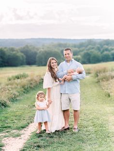 an adult and two children standing on a dirt road in front of a grassy field