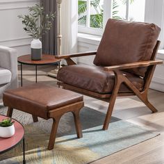 a brown leather chair and foot stool in a living room with a potted plant