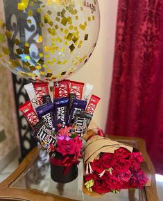 some candy bars and flowers on a table with a large balloon in the background that says happy valentine's day