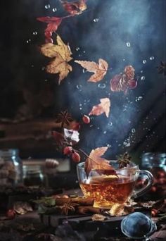 a glass cup filled with liquid and leaves floating in the air on top of a table