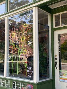 a store front window with flowers drawn on it's glass and painted in green